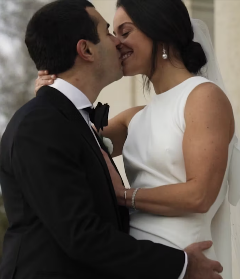 A couple embraces in a tender kiss outdoors, dressed to perfection for a Rittenhouse Hotel New Year's Eve wedding—a vision of elegance with the woman in her pristine white dress and the man looking dapper in his classic black suit.